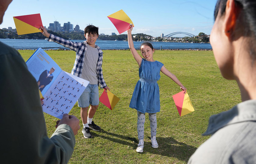 Family on Cockatoo Island using semaphore flags during the family tour, with Sydney Harbour Bridge in the background.