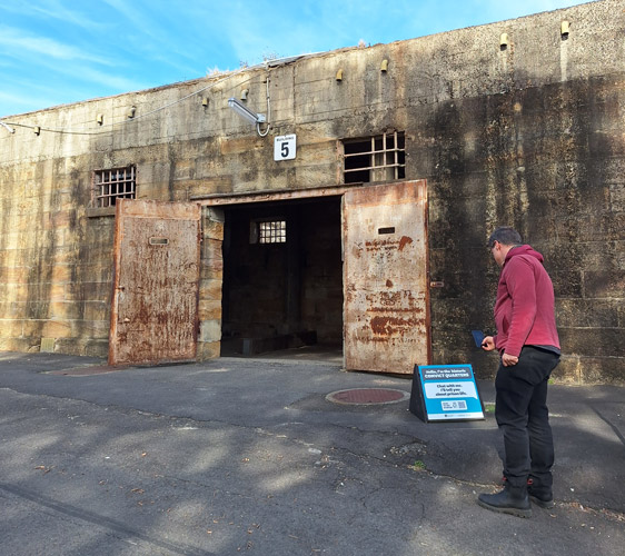 Man using his phone to scan a turquoise talking object sign in the Convict Precinct on Cockatoo Island.