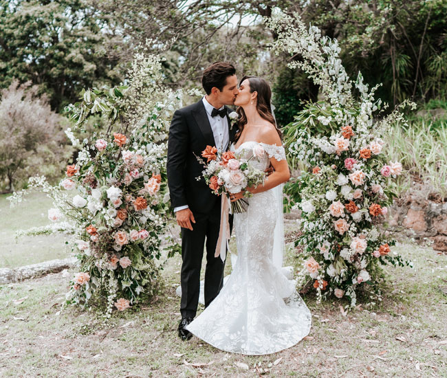 Bride and groom kissing beneath their floral arbor at Burnt Orange.