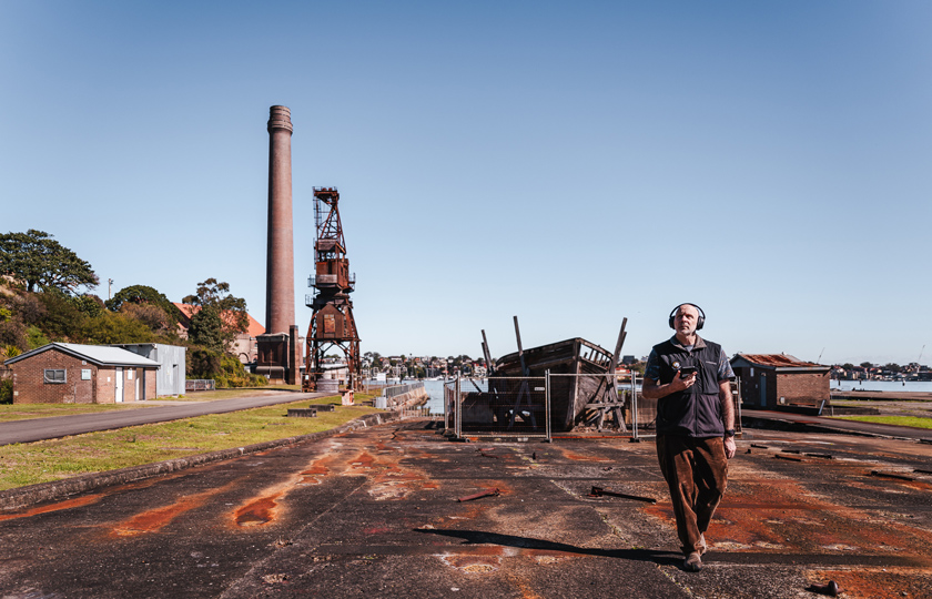 Man enjoying Cockatoo Island's self-guided Audio Tour with the Powerhouse Chimney and Slipways in the background.